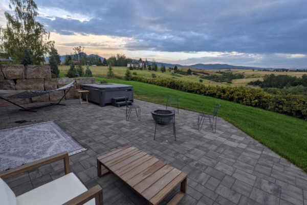 Concrete paver patio with sauna, hot tub and gas fire pit and outdoor dining space in Bozeman Montana